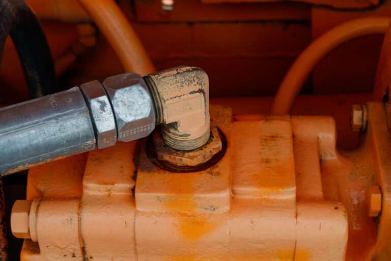 A person examines hydraulic hoses and gauges on machinery in a well-lit garage.