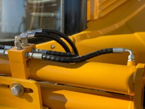 Technician inspecting a cracked hydraulic hose and corroded fittings on outdoor equipment.