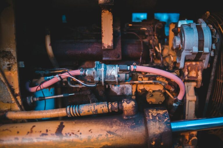 Technician inspecting a noisy hydraulic pump, hoses, reservoir, and pressure lines on industrial equipment.
